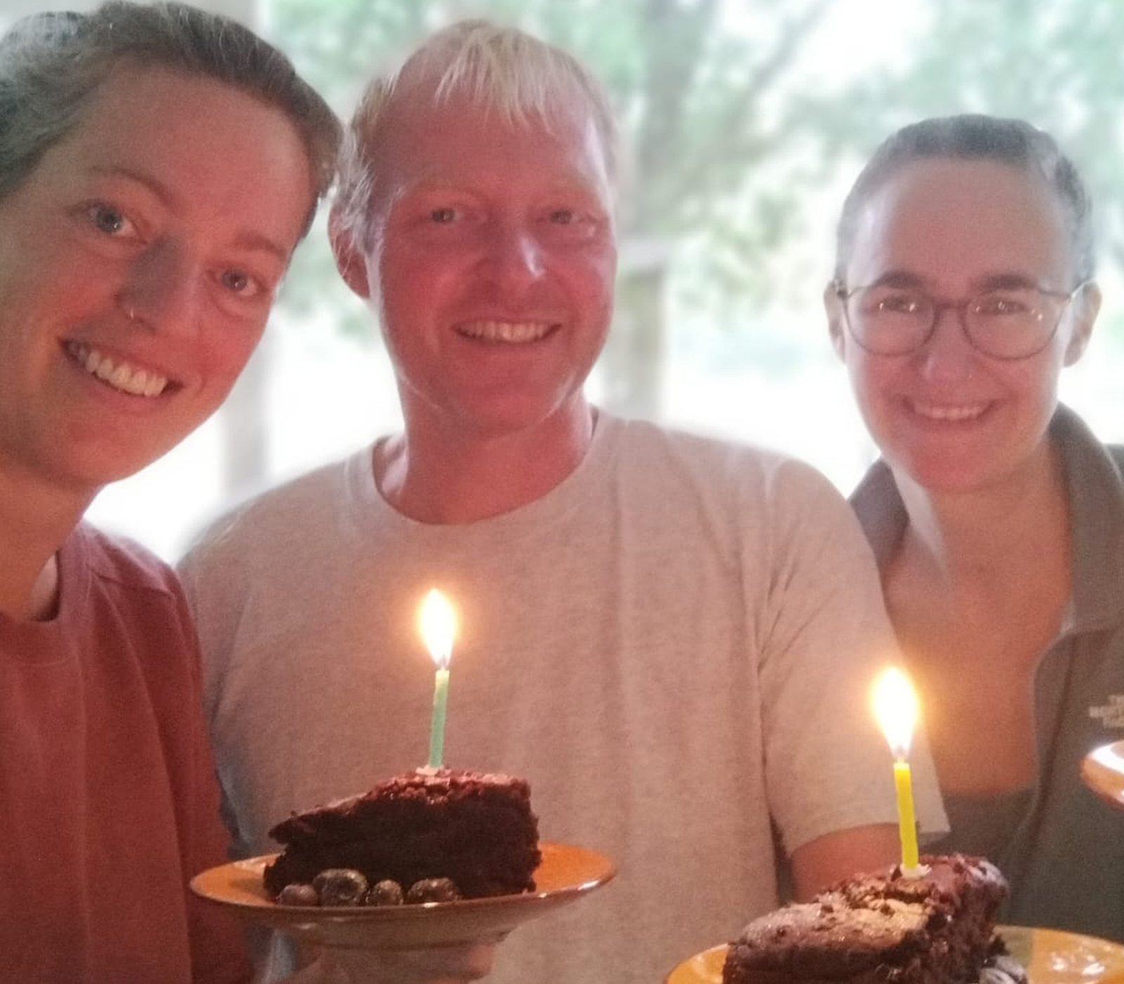 De drie bestuursleden lachend bij elkaar, met taart en brandende kaarsjes