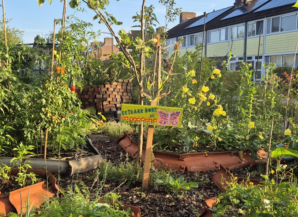 Tuin van Eetbaar Dorp met jonge bomen, bloemen en een bord Eetbaar Dorp